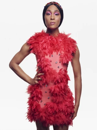 Model wearing a vibrant red feather dress and dark headpiece against a plain white background