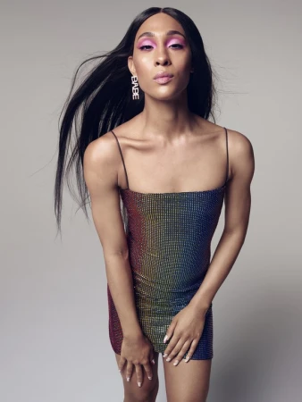 Model in a sequined mini dress with pink eyeshadow and long dark hair against a plain grey background
