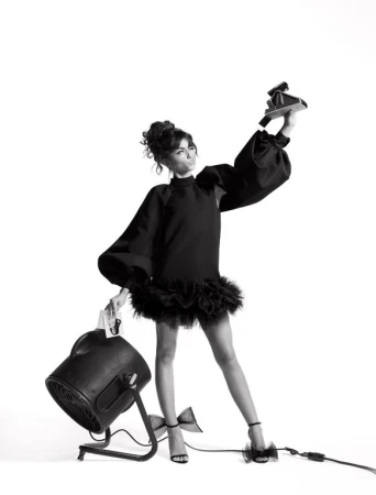 Elegant woman in black dress holding vintage camera and light in a studio fashion shot with a clean white backdrop, glamorous and stylish.