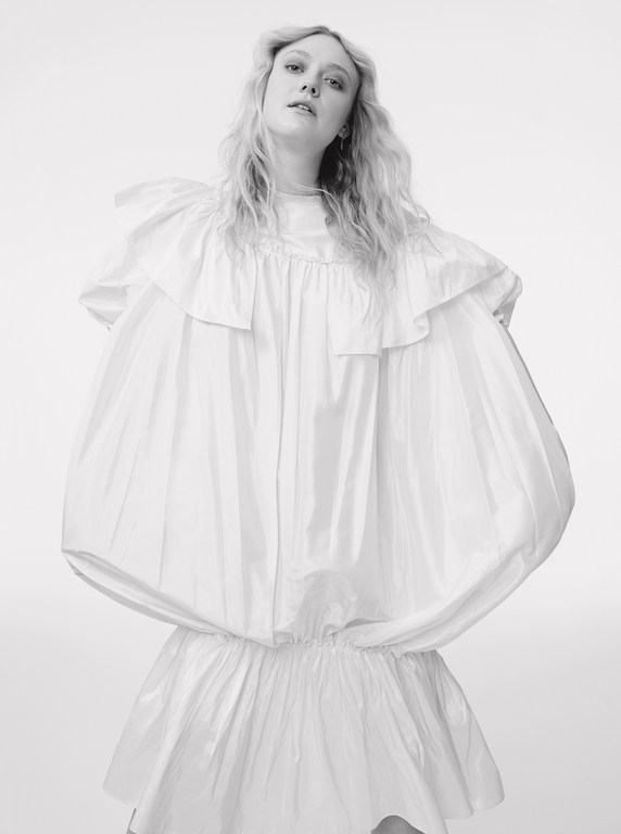 Portrait of blonde woman wearing a voluminous white ruffled dress against a plain light background