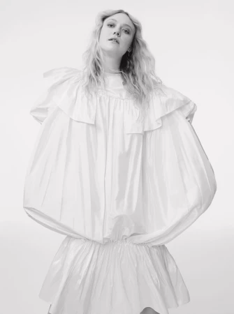 Portrait of blonde woman wearing a voluminous white ruffled dress against a plain light background
