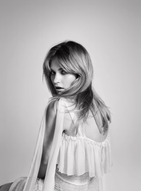 Black and white portrait of an adult female with blonde hair, wearing a ruffled white dress, looking over her shoulder with an open mouth.