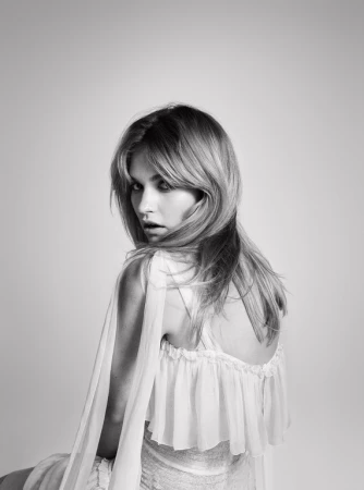 Black and white portrait of an adult female with blonde hair, wearing a ruffled white dress, looking over her shoulder with an open mouth.