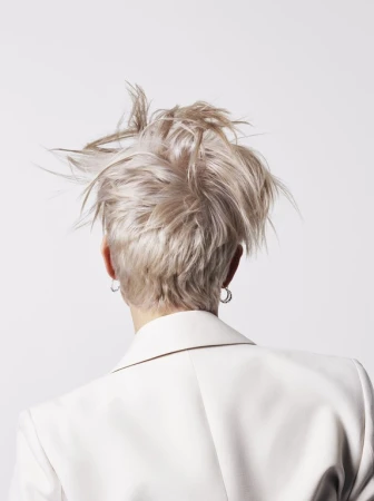 Rear view of a person with tousled blonde hair wearing a white blazer against a white background.