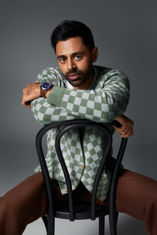 Portrait of a man in a checkerboard cardigan sitting on a chair. The photo is taken in a studio with soft, diffused lighting.