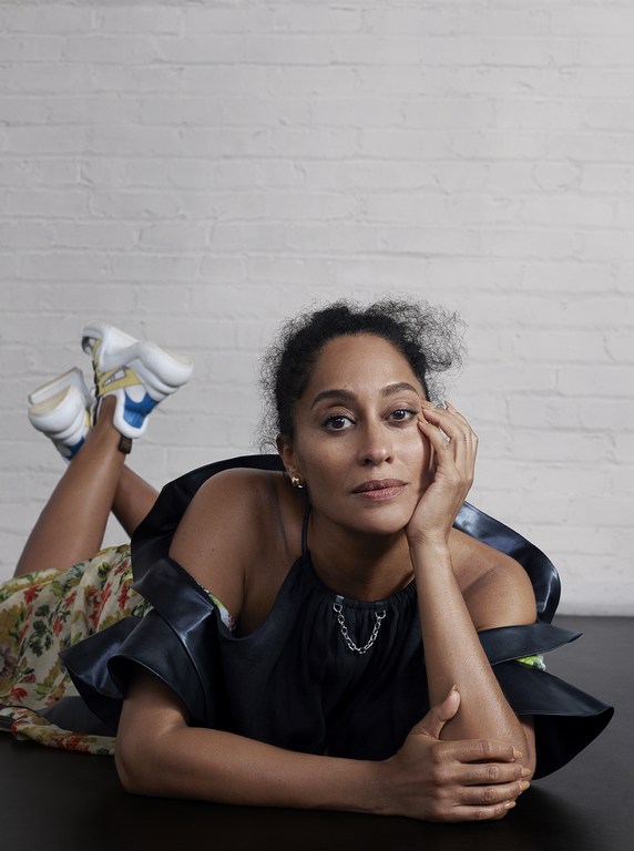Woman in dark halter top lying on floor with legs kicked up against white brick wall