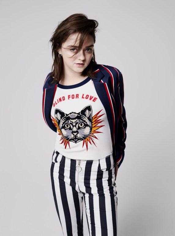 Young woman in a striped blazer poses in a photo studio wearing an animal graphic tee and striped pants with a neutral backdrop.