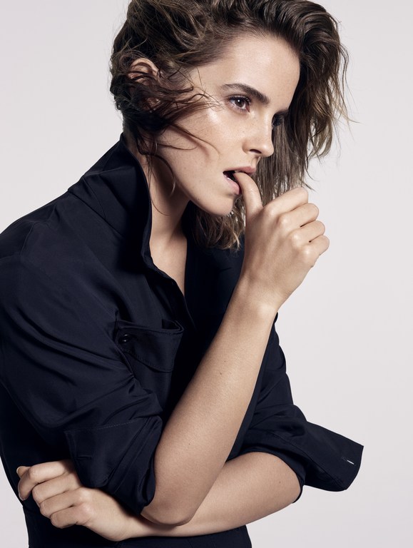 Emma Watson poses in a close-up, side-profile shot, wearing a black button-down shirt against a clean, bright backdrop.