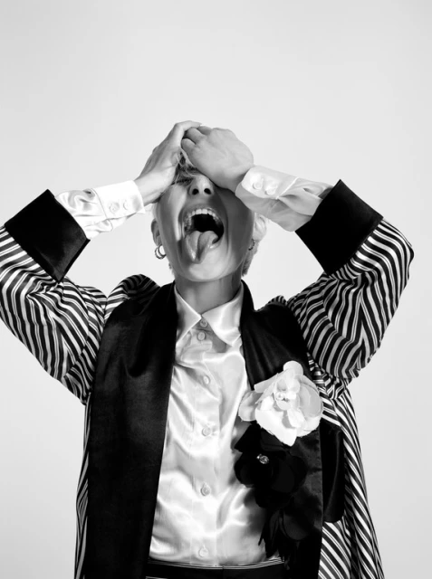 Striking black-and-white portrait of a woman with a short haircut, wearing a striped jacket and silk shirt, expressing frustration.