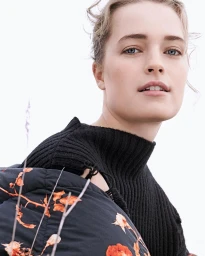 Close-up portrait of a woman wearing a black ribbed sweater and floral puffer jacket by Kerry Hallihan