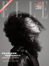 Black and white portrait of Alicia Keys with voluminous curly hair wearing a dark leather jacket against a grey background.