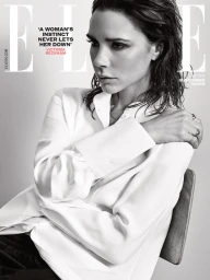 Victoria Beckham wearing a white button-down shirt seated on a chair against a plain light grey background