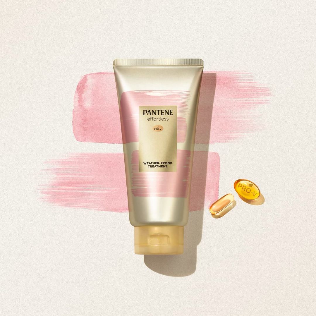 Close-up studio shot of Pantene Effortless Weather-Proof Treatment product, with Pro-V capsules, against a pink watercolor background.
