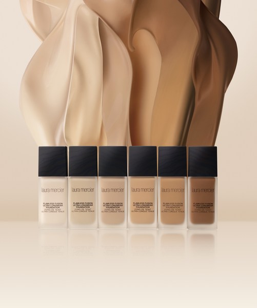 Laura Mercier Flawless Fusion Foundation in a range of shades against tan and brown smears in a studio shot.