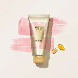 Pantene tube product photography against pale textured background with pink brush strokes and golden oil capsules by Magnus Cramer