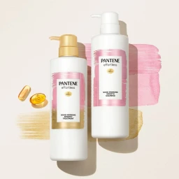 Two white shampoo and treatment bottles with pink and gold labels standing against a cream background with watercolor brush strokes.