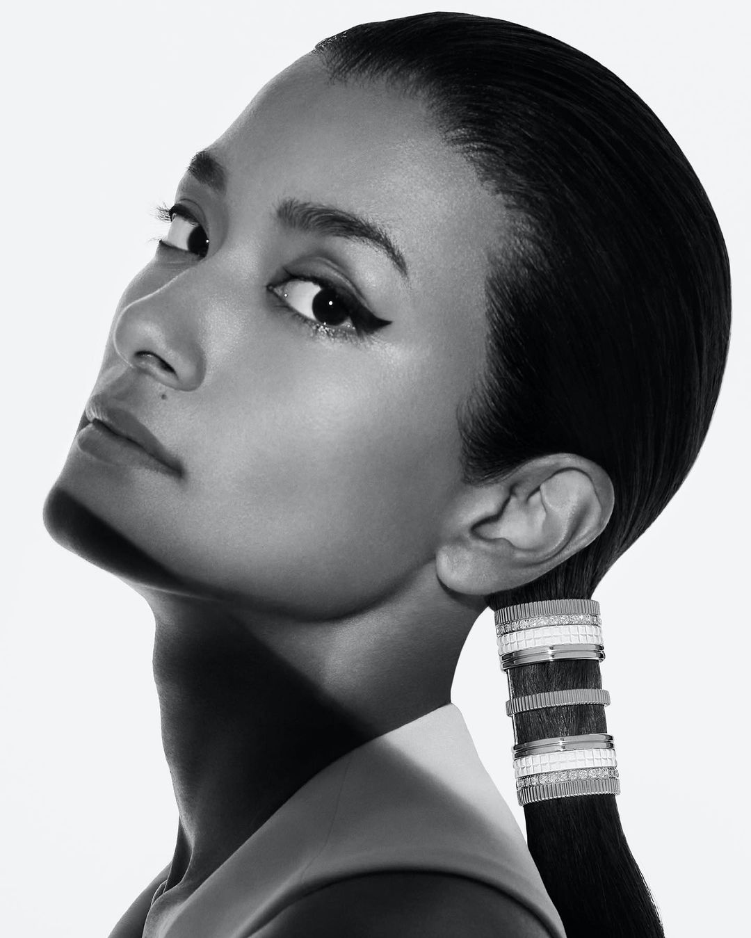 Black and white close-up shot of a woman with sleek hair and jewelry, showcasing her profile against a clean, light backdrop.