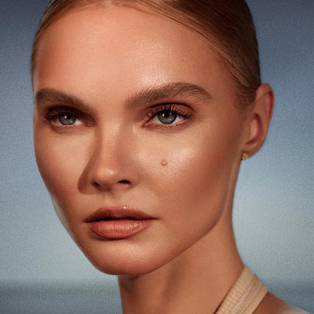 Close-up portrait of a fair-skinned woman with blonde hair pulled back, showcasing natural makeup and a calm expression against a blue gradient.
