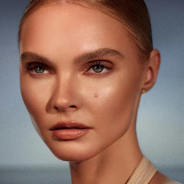 Close-up portrait of a fair-skinned woman with blonde hair pulled back, showcasing natural makeup and a calm expression against a blue gradient.