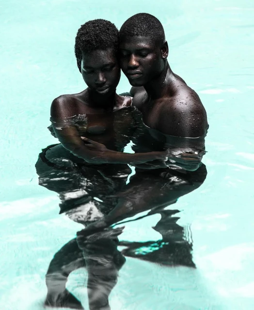 Striking studio portrait of a Black couple in water, embracing closely with a light blue background, creating a sense of intimacy and connection.