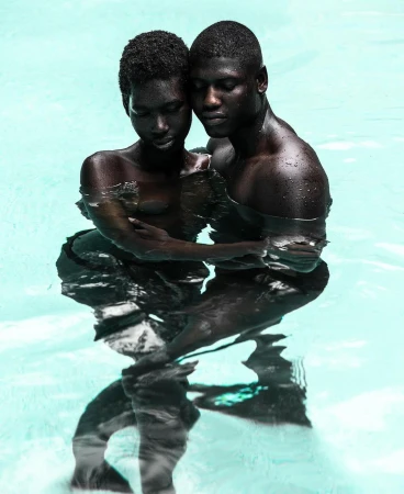Striking studio portrait of a Black couple in water, embracing closely with a light blue background, creating a sense of intimacy and connection.