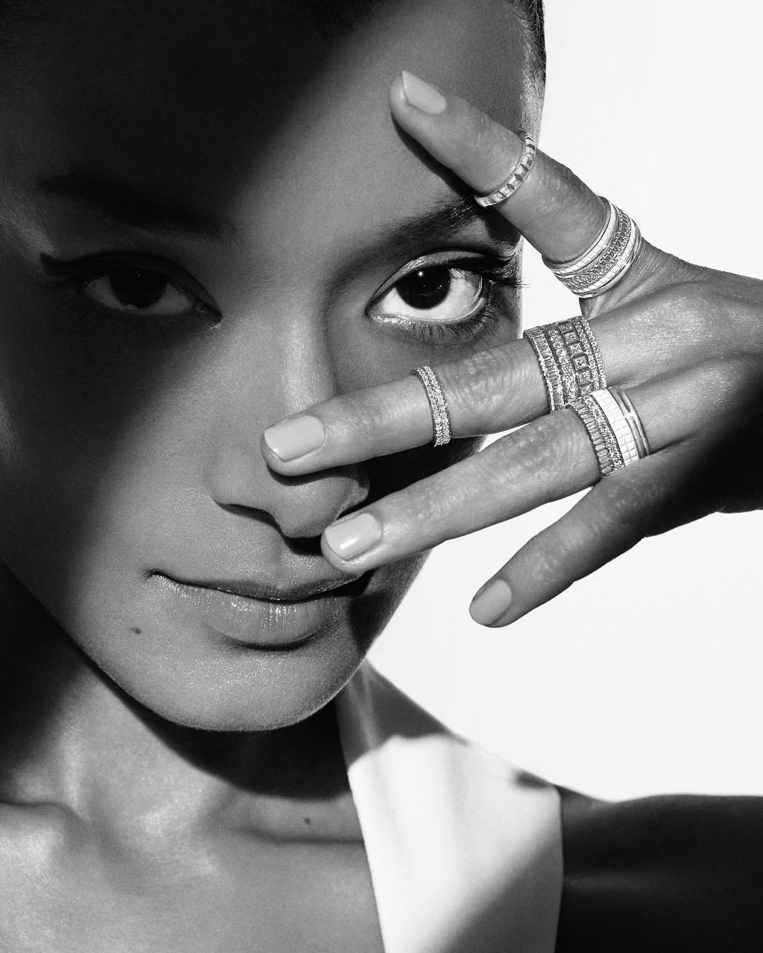 Elegant portrait of a woman showcasing an array of rings on her fingers, partially obscuring her face, in a monochrome color palette.