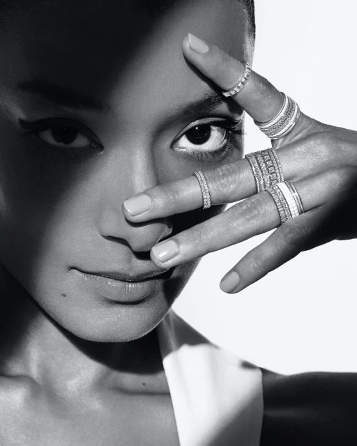 Elegant portrait of a woman showcasing an array of rings on her fingers, partially obscuring her face, in a monochrome color palette.
