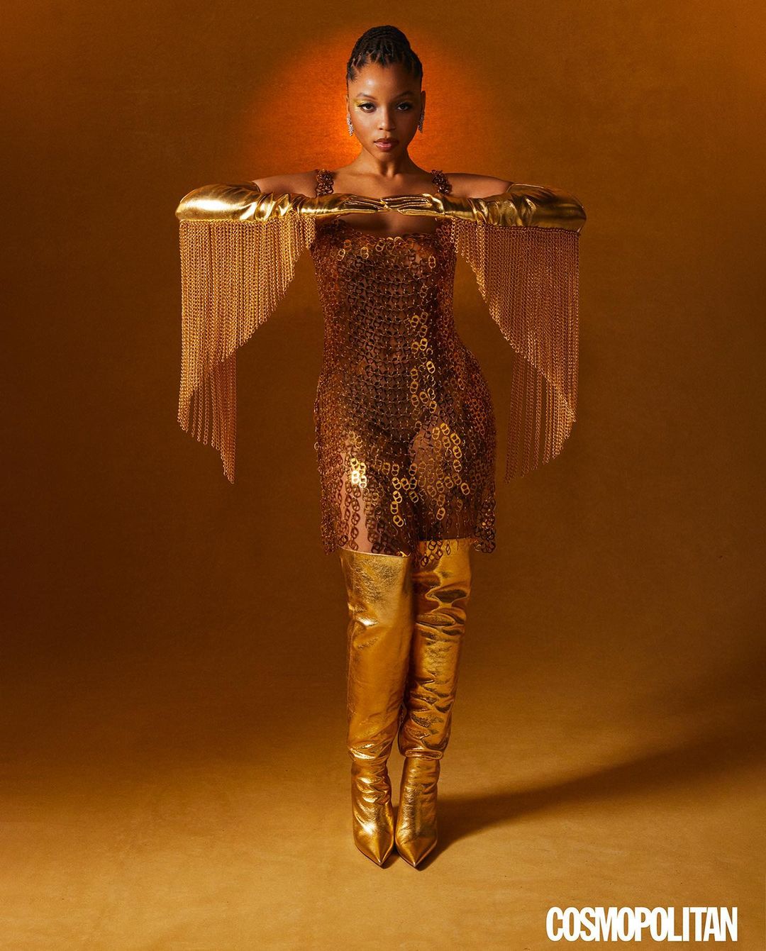 A woman poses in a gold dress and thigh-high gold boots against a gold background, radiating confidence and style for a photoshoot.