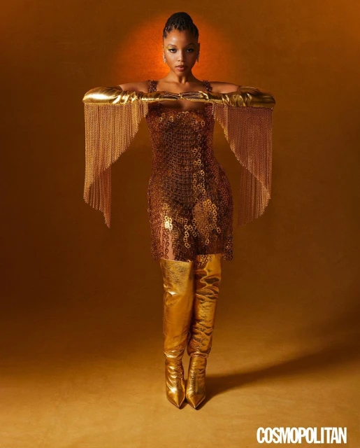 A woman poses in a gold dress and thigh-high gold boots against a gold background, radiating confidence and style for a photoshoot.