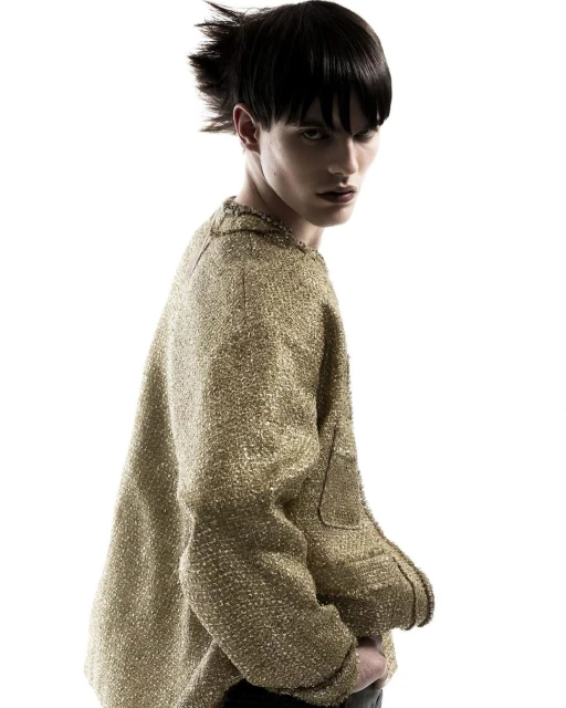Fashion portrait of a male model in a gold tweed jacket against a white background with dramatic hair and makeup.
