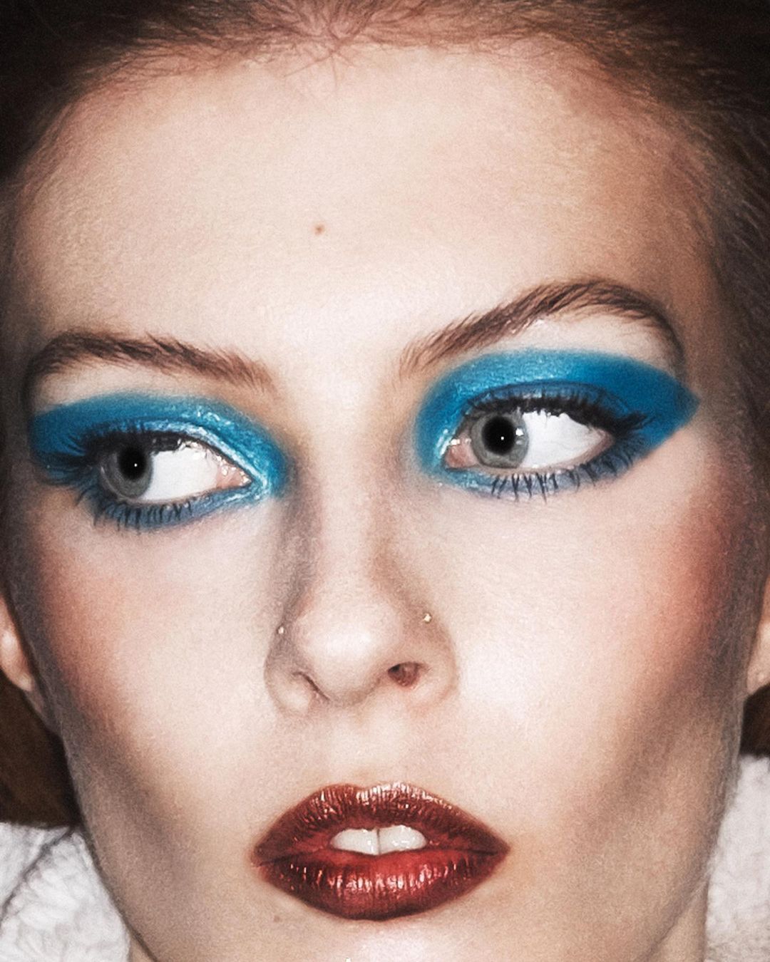 Close-up portrait of a woman with vibrant blue eyeshadow and metallic dark red lipstick photographed by Marcus Cooper.