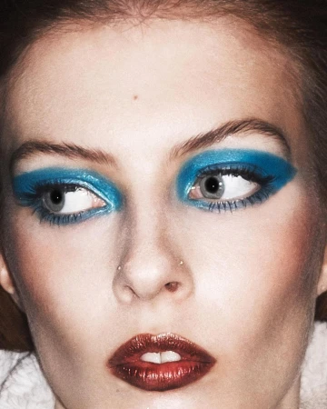 Close-up portrait of a woman with vibrant blue eyeshadow and metallic dark red lipstick photographed by Marcus Cooper.