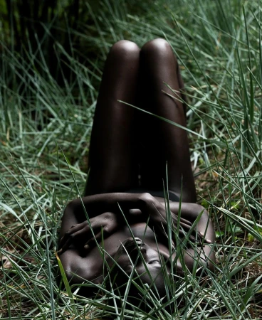 Black woman lying among tall green grass with her knees drawn upward