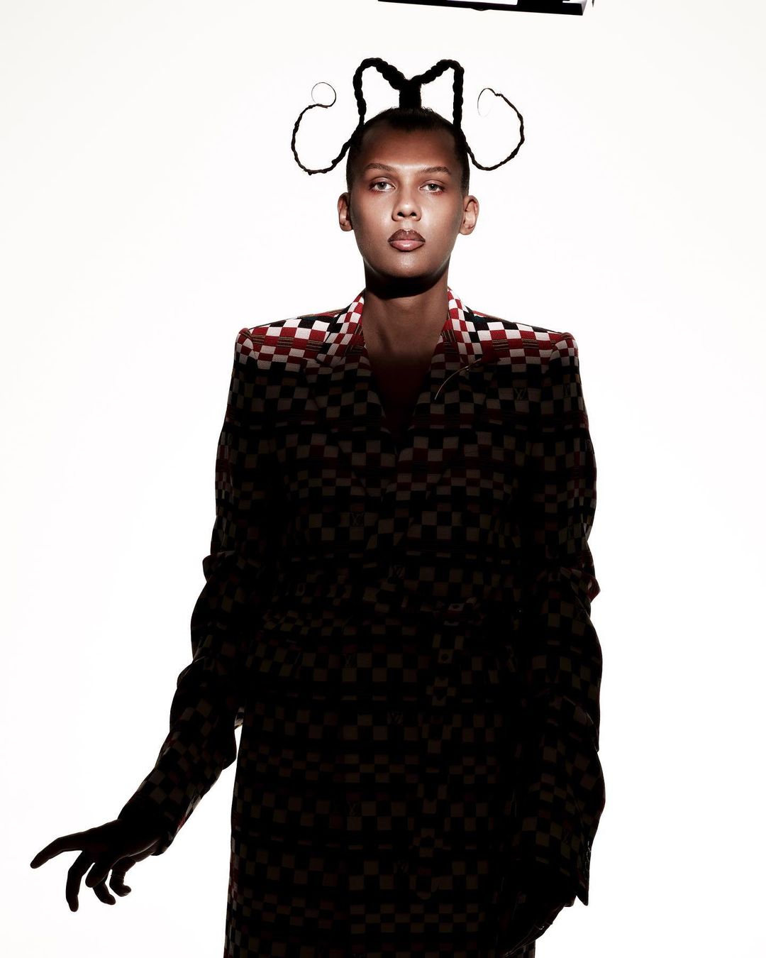 Model in a checkered patterned coat with elaborate sculptural braided hair against a plain white background