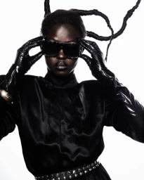Black woman in a black satin top wearing sunglasses and leather gloves against a white background