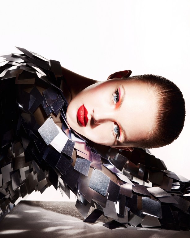 Woman in metallic silver outfit with red lips poses against a white backdrop in this beauty and fashion portrait.