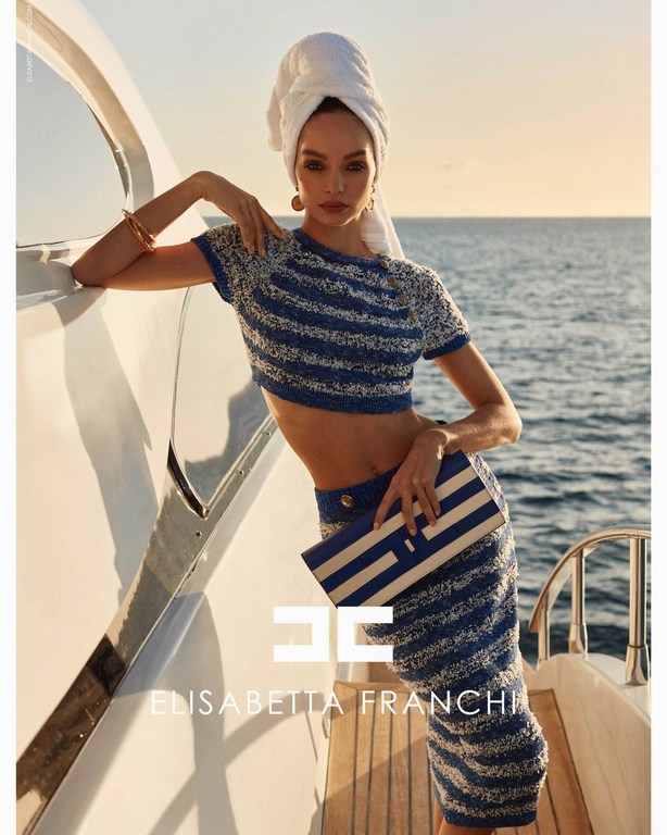 Fashion shot of a model on a yacht, wearing blue and white striped matching set with a white towel on her head and a clutch.
