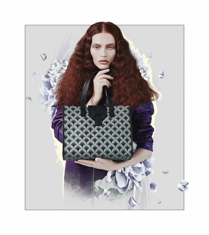 Adult female model in a studio holding a handbag with a patterned design, wearing a purple jacket against a floral background.