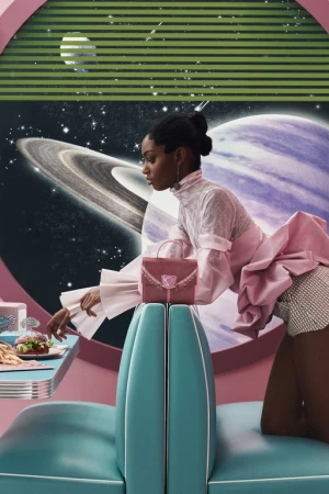 Glamorous Black female model poses in a retro-futuristic diner setting with space scene backdrop, showcasing a pink handbag.
