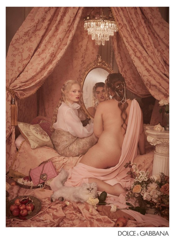 Fashion editorial featuring two women in an boudoir, one nude draped in pink fabric, accompanied by a white Persian cat. Dolce & Gabbana ad.