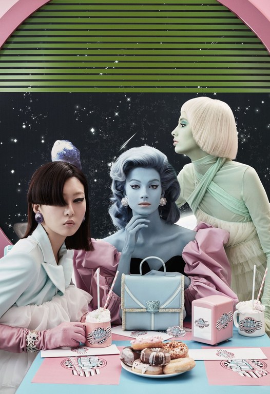 Three women with blue, green and brown skin tones wearing retro fashions sit at a pink and blue table with donuts and milkshakes.