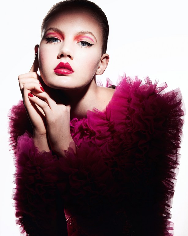 Portrait of a fair-skinned young adult female model with pink eye shadow and lipstick, wearing a ruffled magenta tulle top.