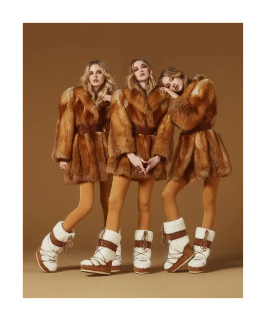 Three fashion models pose in matching brown fur coats, tan leggings, and white moon boots on a monochromatic tan backdrop.