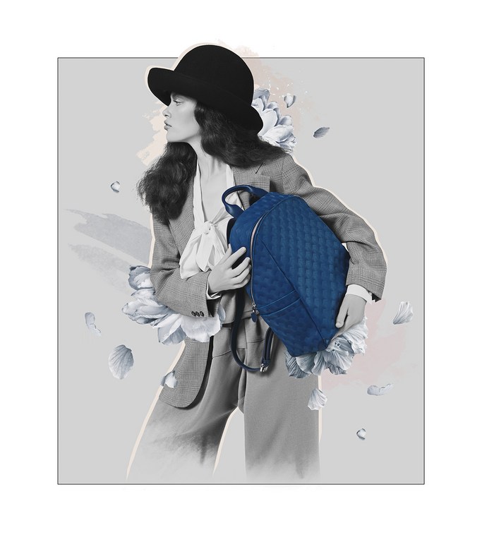 A woman in a suit and hat holds a quilted blue backpack in a digitally enhanced studio image featuring abstract floral elements.