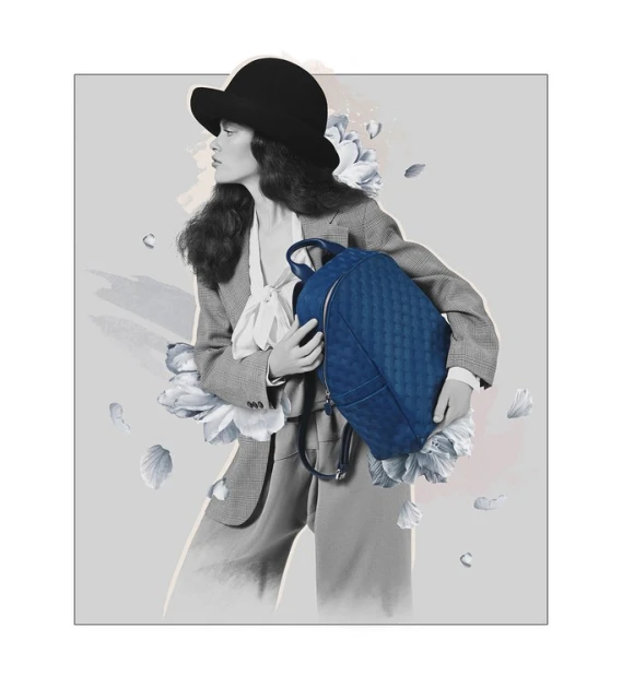 A woman in a suit and hat holds a quilted blue backpack in a digitally enhanced studio image featuring abstract floral elements.