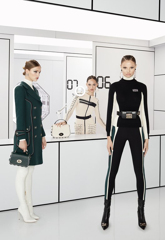 Three fashion models in a bright white space pose in front of a backdrop with geometric shapes and digital-style numbers, showcasing apparel.