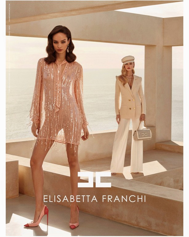 Two fashion models wearing outfits by Elisabetta Franchi. One model wears a sequin dress and the other a tailored suit.