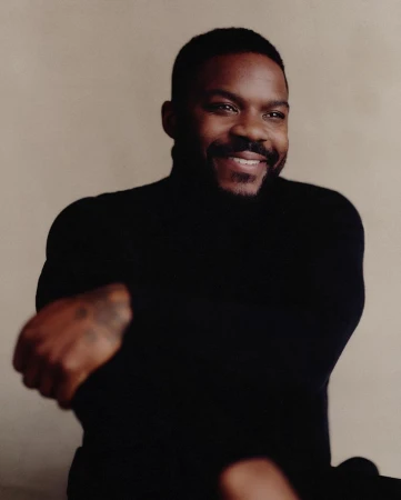 Portrait of smiling Black man in his 30s wearing a black turtleneck sweater against a neutral background by Pip