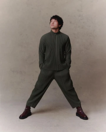 Portrait of an adult man in pleated matching set with brown ankle boots looking upwards in a studio setting with a neutral background.