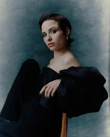 A dark-haired woman in a black strapless top seated against a textured grey studio backdrop, photographed by Pip in London.